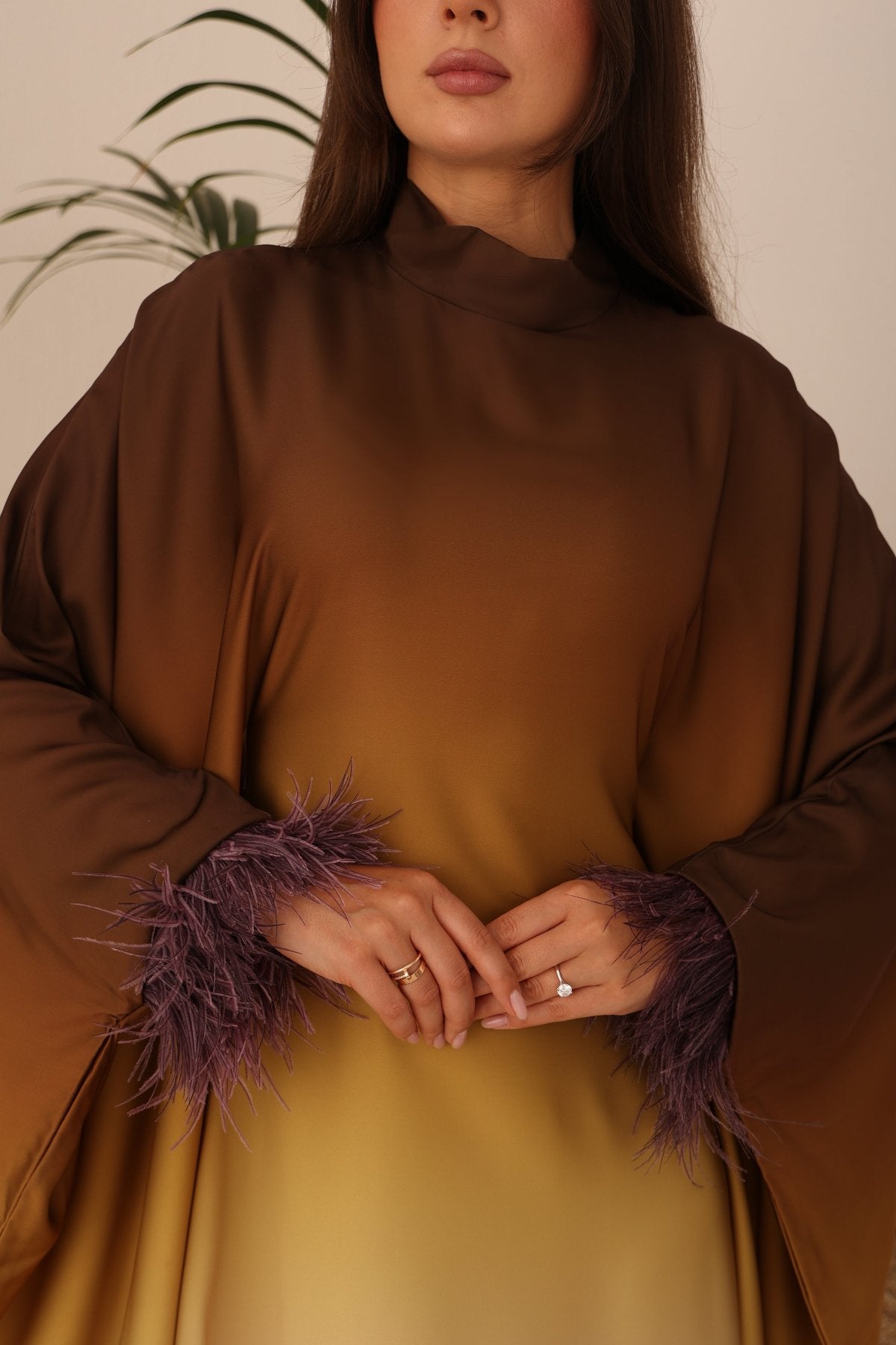 Close-up of the feathered sleeve details on the luxurious satin Sahara Glow Kaftan, highlighting its ombré brown-to-gold color palette.