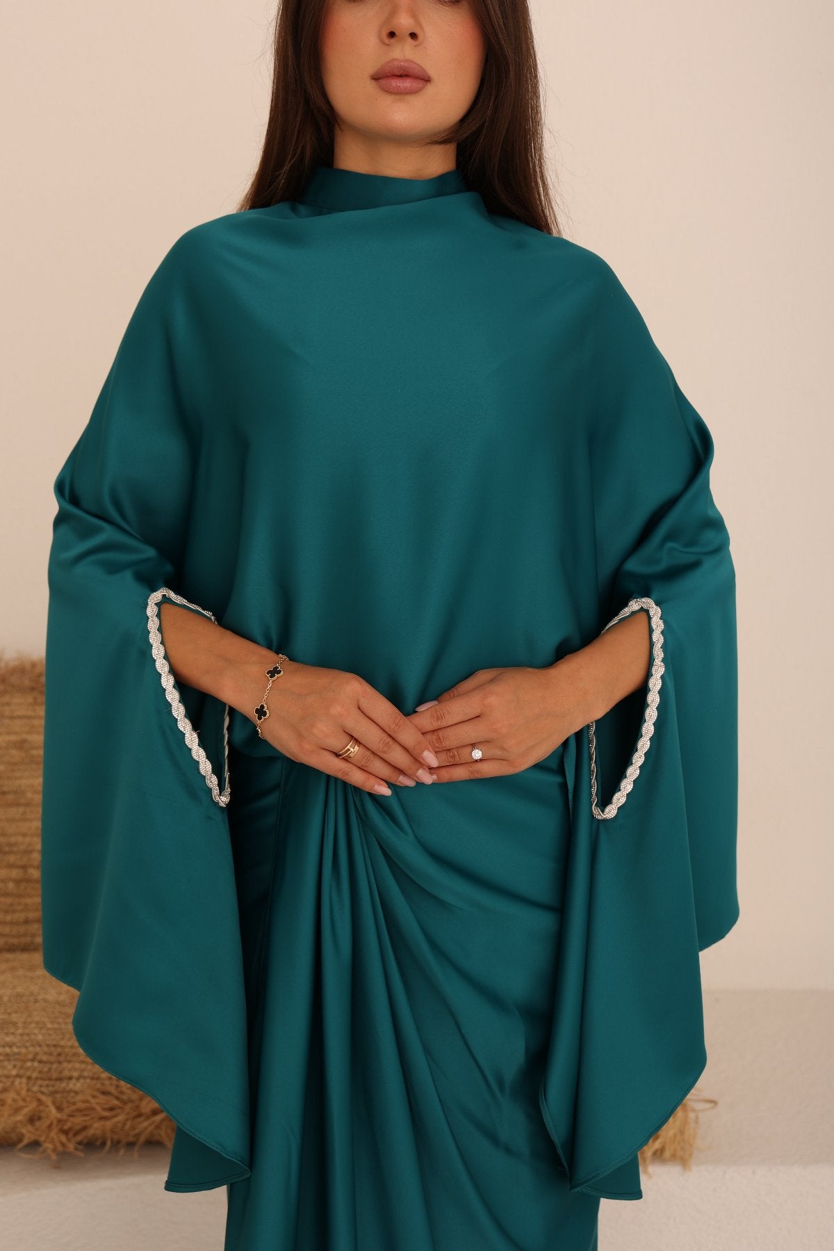 Close-up of teal satin wrap skirt with embellishment details on batwing sleeves.